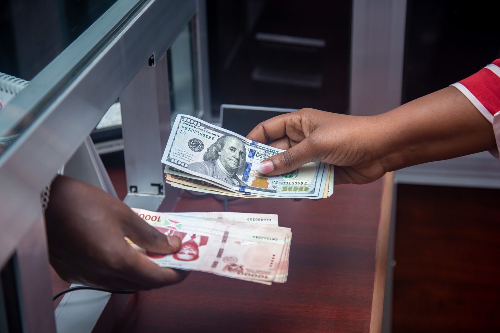 Hands exchanging US dollar bills and local currency across a counter, representing a cross-border remittance transaction